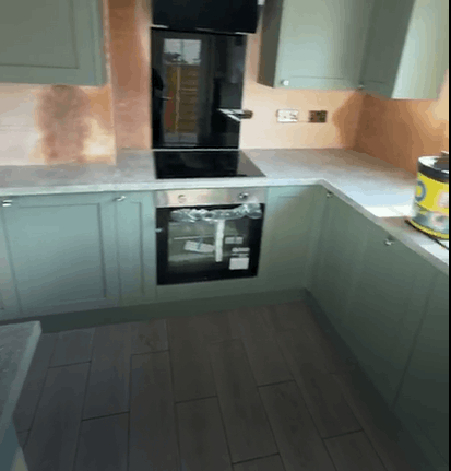 Modern kitchen floor installation featuring grey wood-effect tiles, sage green cabinets, and a stylish fitted kitchen design.